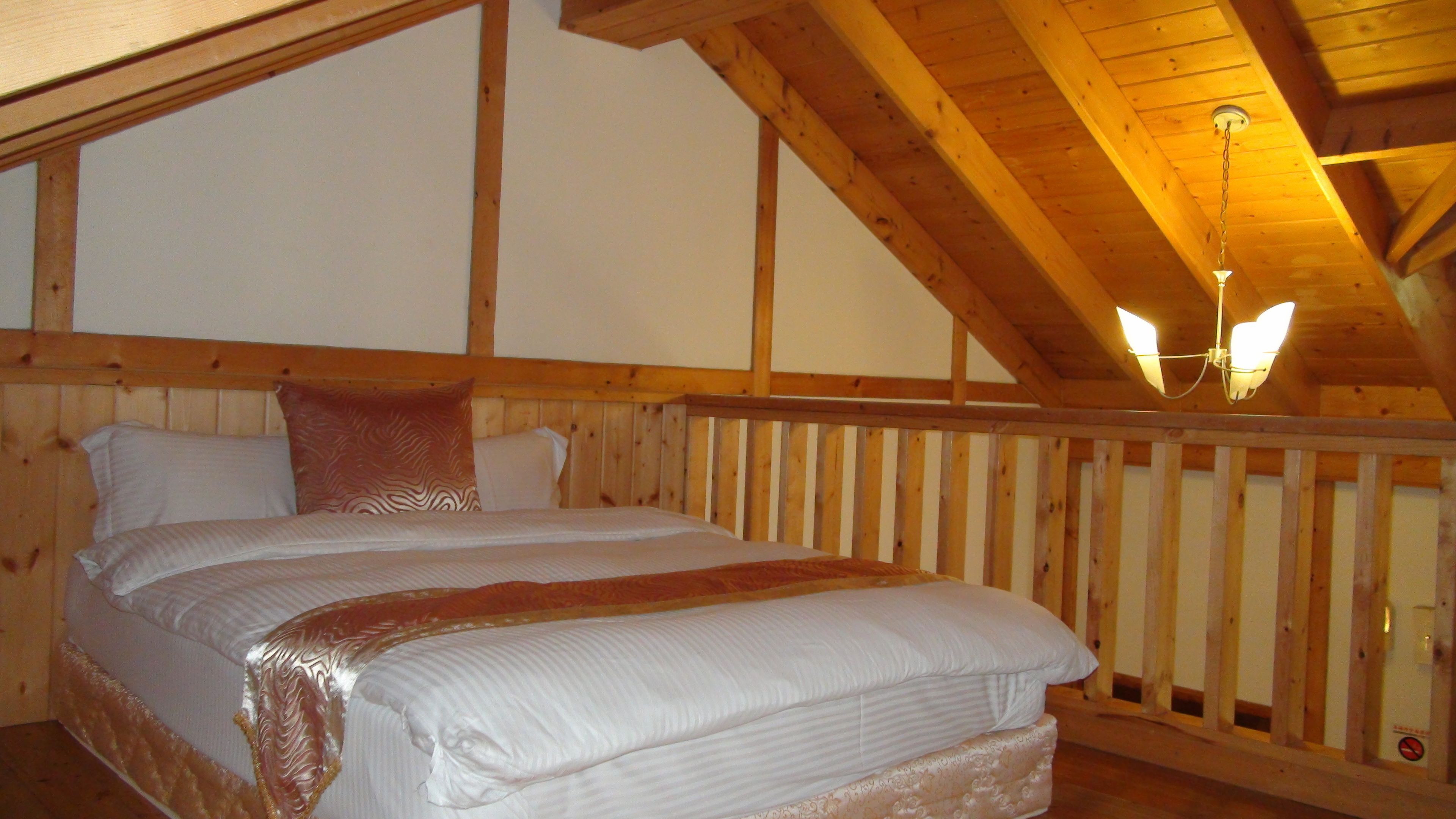 A wooden-framed room with a bed, a chandelier, and a view of the outdoors.