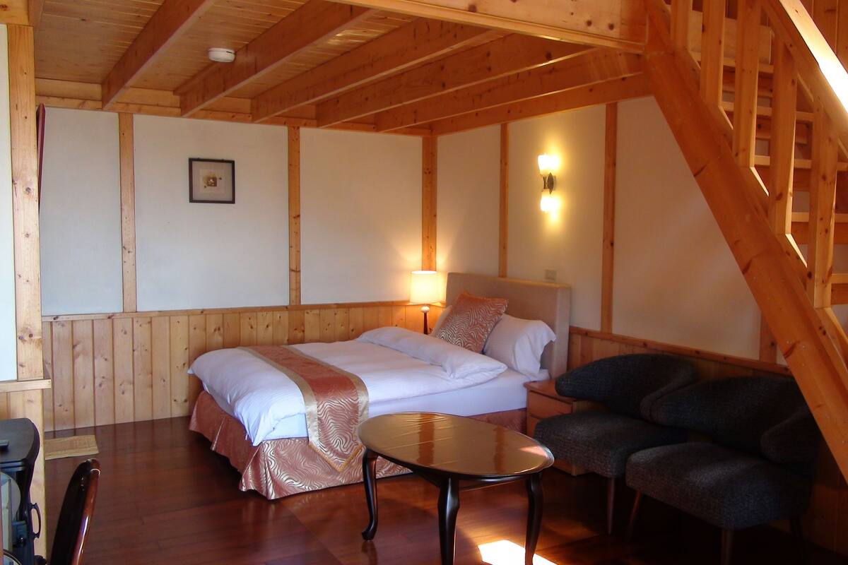 A cozy room with a bed, two bedside tables, a chair, and a wooden staircase.