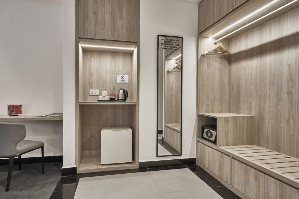 Une chambre d’hôtel équipée d’un bureau, d’un miroir, d’un petit réfrigérateur et d’une étagère sur laquelle se trouve un appareil photo.