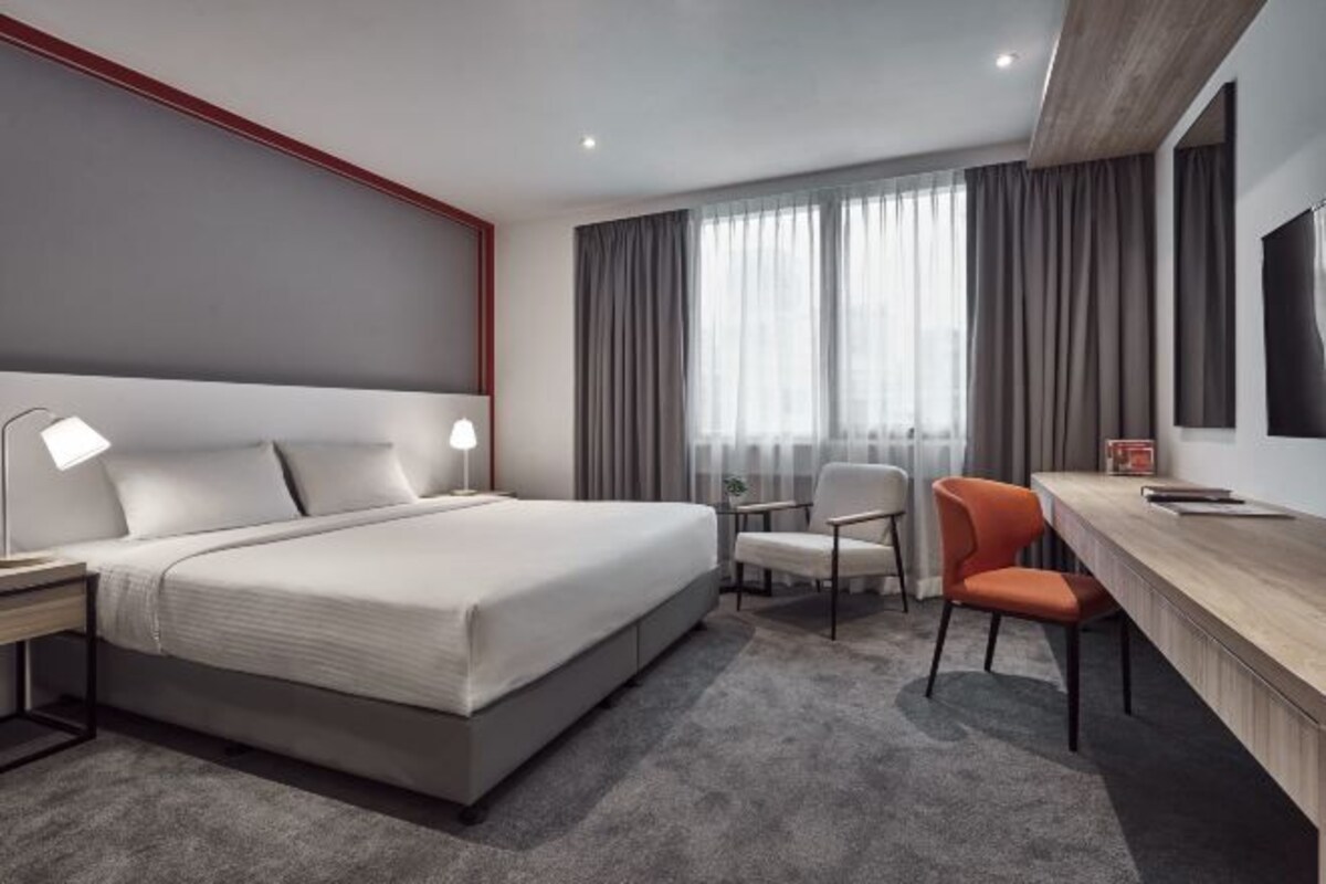 Une chambre d’hôtel moderne avec un grand lit, deux fauteuils, un bureau et une télévision.