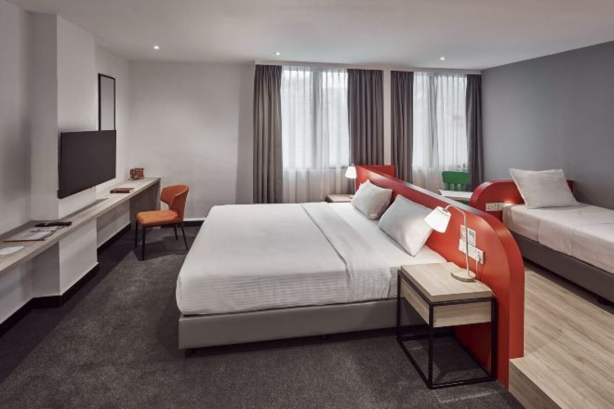 Une chambre d’hôtel moderne, dotée d’un grand lit, d’un bureau avec une chaise, d’une télévision et d’une fenêtre avec des rideaux.
