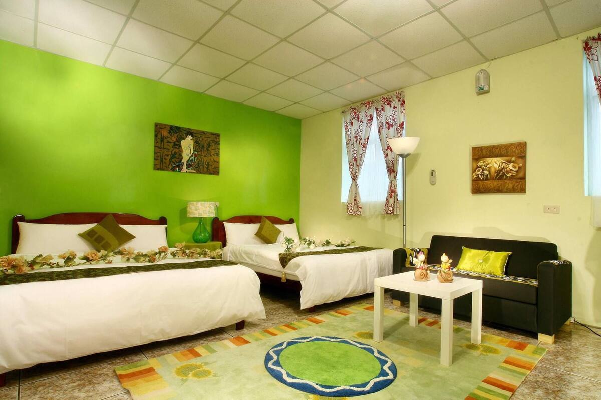 Une chambre d’hôtel avec deux lits, un canapé, une table basse et un tapis coloré.