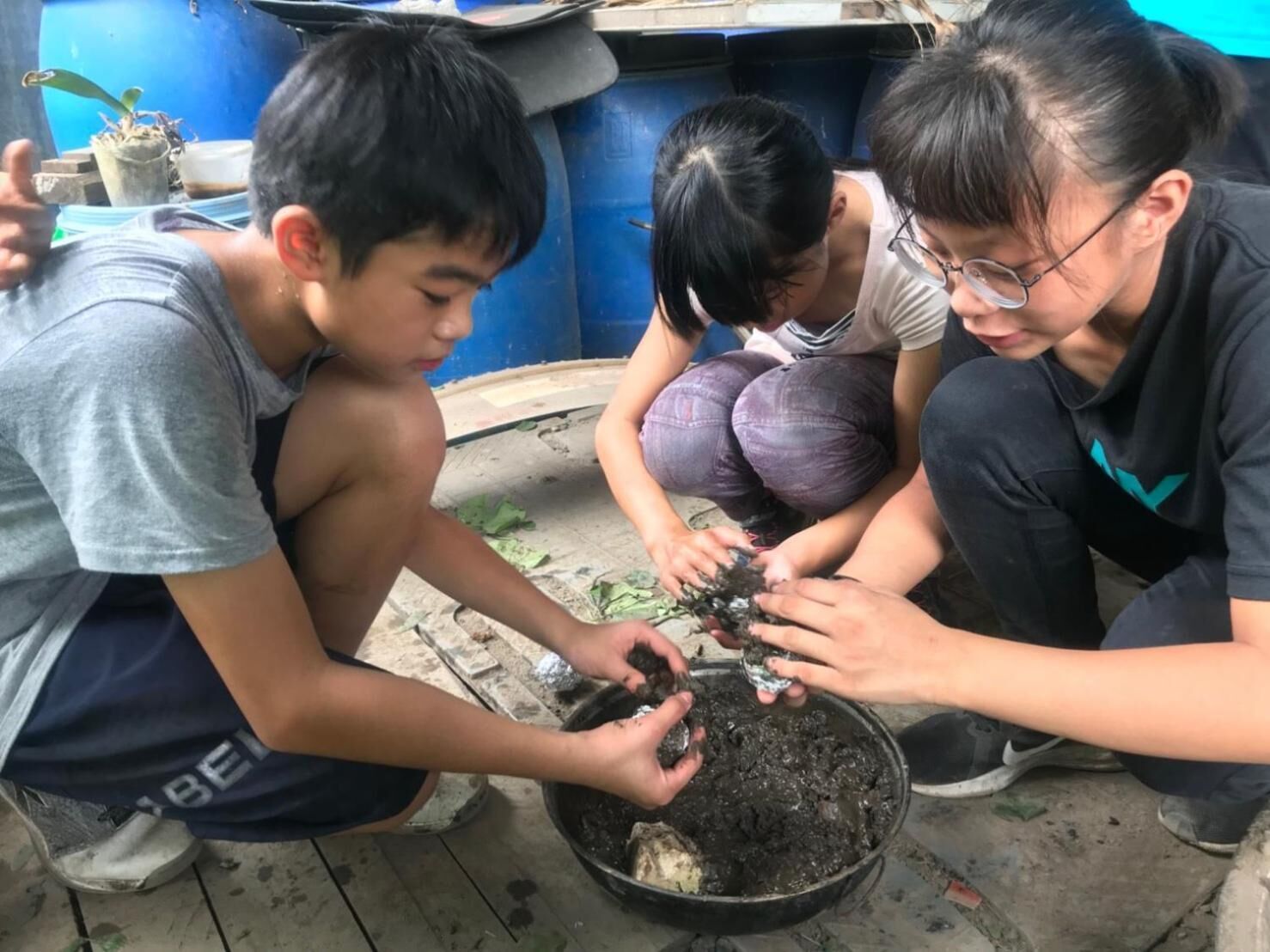 Three individuals engaged in an activity with soil and plants in a rustic outdoor setting.