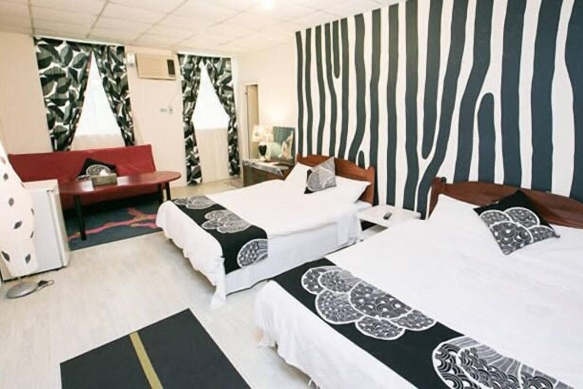 Une chambre d’hôtel avec deux lits, un canapé rouge, un bureau et un mur à rayures zébrées.