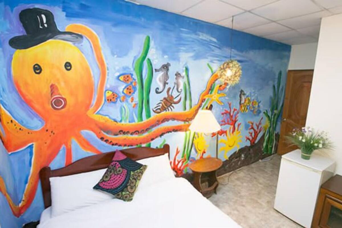Une chambre à coucher avec une fresque représentant une pieuvre, un lit, une table de chevet et une lampe.