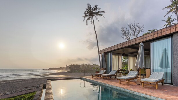 A pool area with lounge chairs and a view of the beach at sunset. - Balian Surf Villas (Selemadeg)