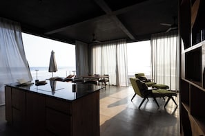 A modern room with a large window, a dining area, and a seating area with a view of the sea. - Balian Surf Villas (Selemadeg)