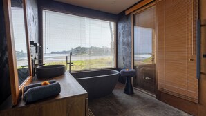 A modern bathroom with a freestanding bathtub, a wooden vanity, and large windows offering a view of the outdoors. - Balian Surf Villas (Selemadeg)