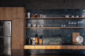 A modern kitchen with wooden cabinets, a stainless steel refrigerator, and a black backsplash. - Balian Surf Villas (Selemadeg)