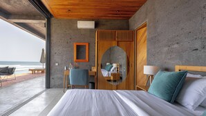 A bedroom with a large bed, a wooden wardrobe, a desk with a chair, and a view of the ocean. - Balian Surf Villas (Selemadeg)
