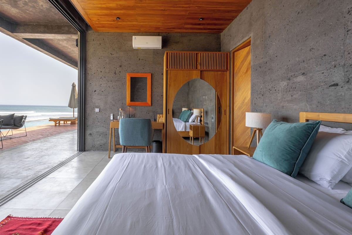 A bedroom with a large bed, a wooden wardrobe, a desk with a chair, and a view of the ocean.