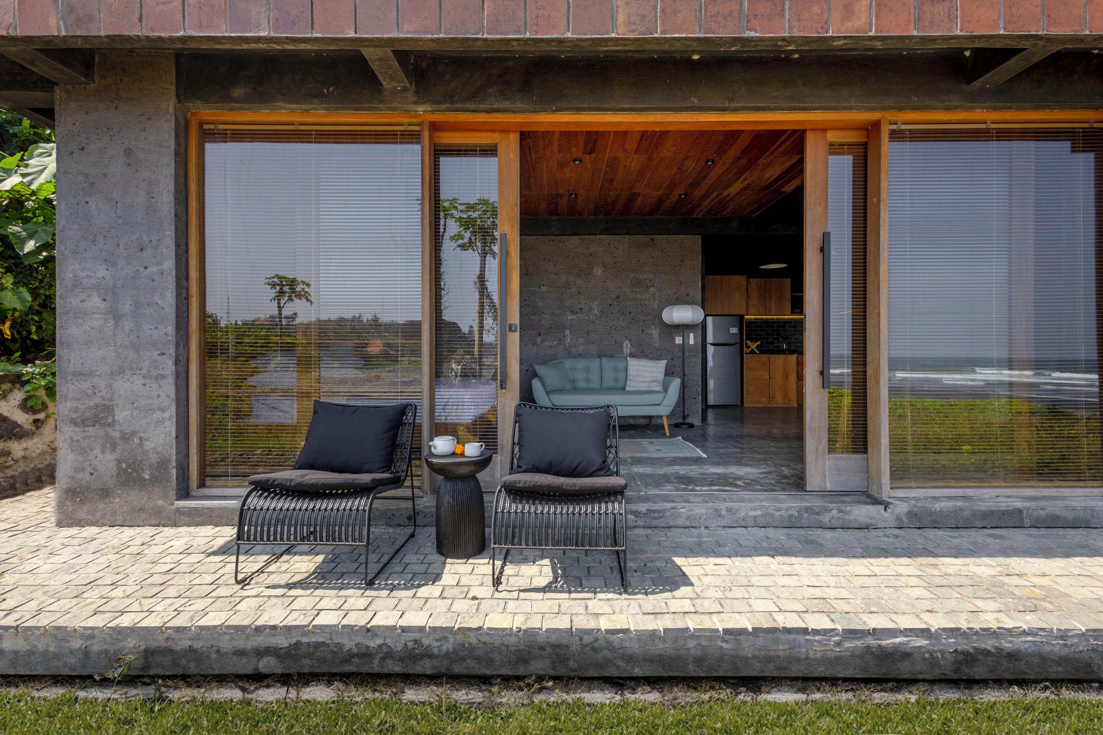 Un espace de détente extérieur moderne, doté de deux chaises et d’une table, avec une structure en béton et une vue sur l’intérieur.