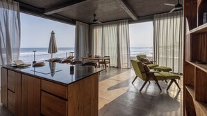 A modern room with a large window overlooking the ocean, a wooden desk, and comfortable seating. - Balian Surf Villas (Selemadeg)