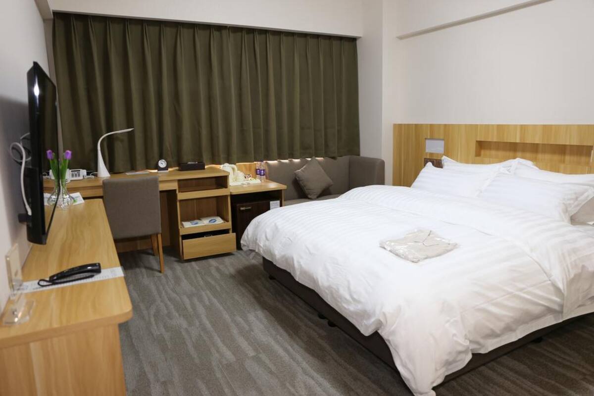 Ein Hotelzimmer mit einem Bett, einem Schreibtisch mit Stuhl, einem Fernseher und einem Fenster mit Vorhängen.