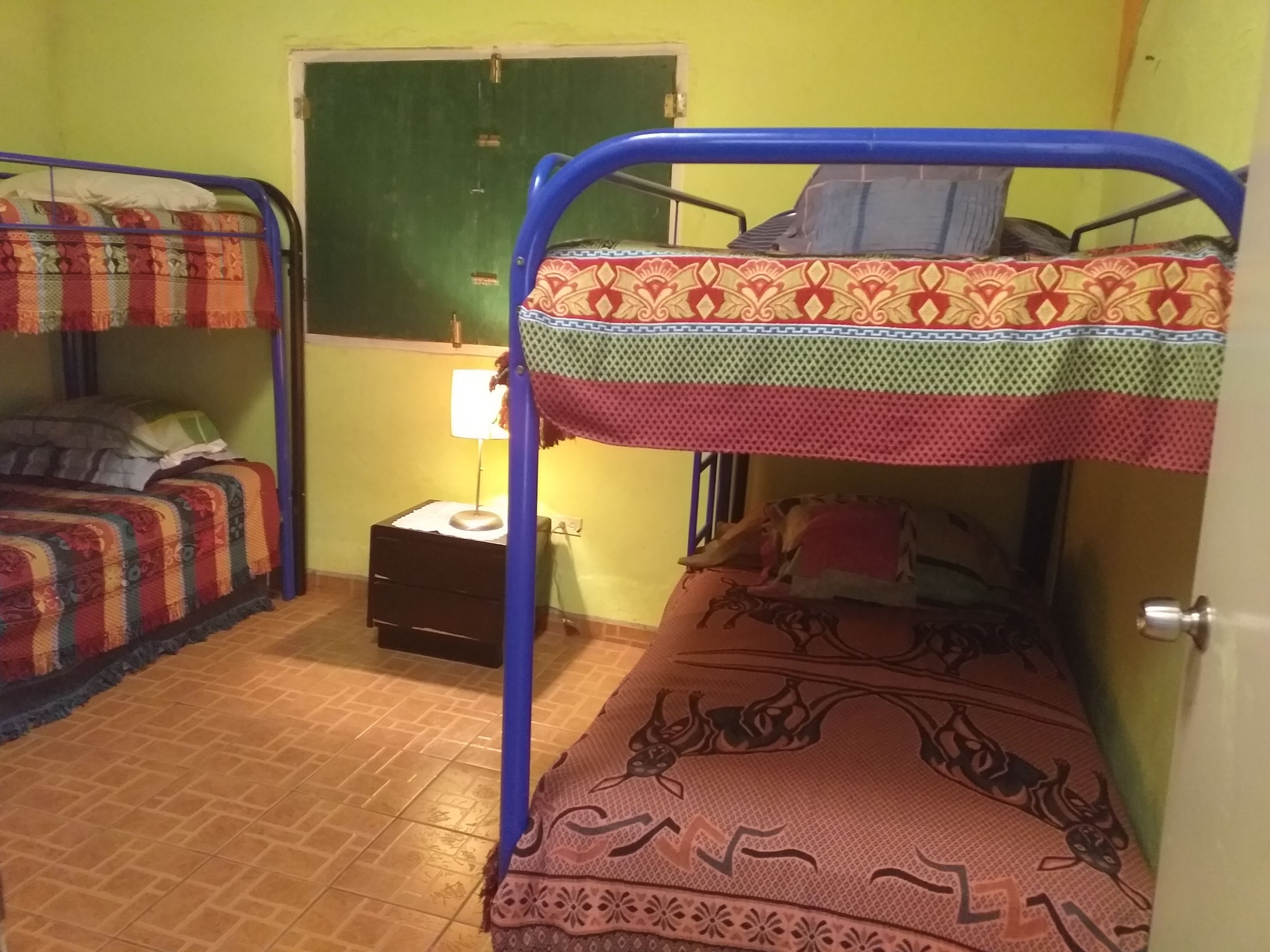Una habitación con dos literas, una mesita con una lámpara y una puerta verde.