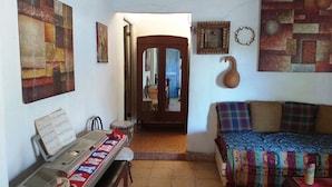 A room with a wooden bench, a sofa, and a tiled floor. There are paintings on the walls and a door leading to another room. - La Casita de Don Daniel (El Valle de Anton)