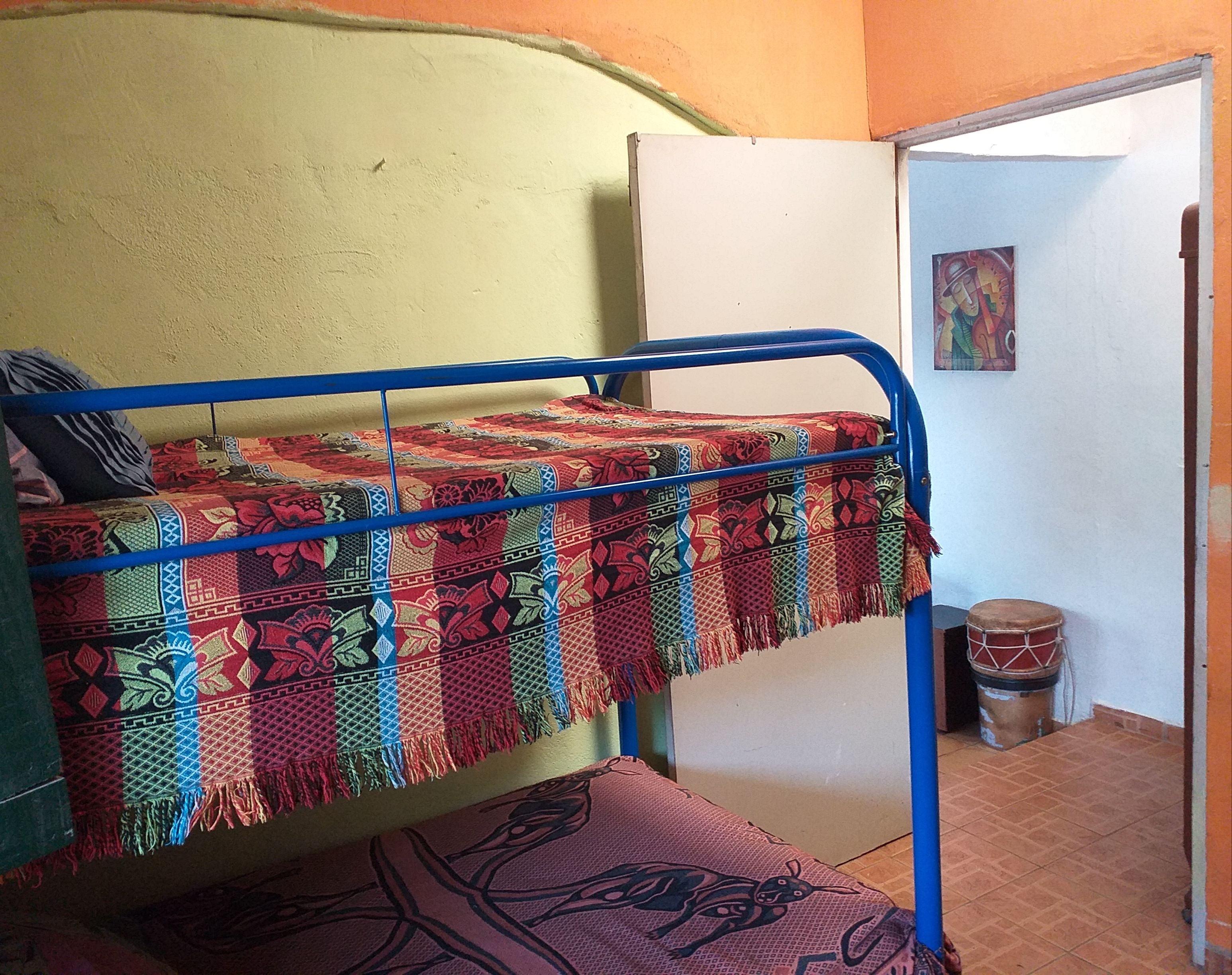 Una cama individual con un edredón colorido, una batería y un cuadro en la pared.