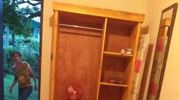 Una camera da letto con un'armadio in legno, una ventola a piantana e un letto con copripiumino a motivi floreali.