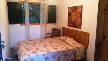 A bedroom with a bed, a chair, a window with a curtain, and a wall-mounted artwork.