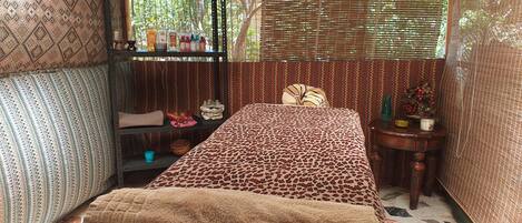 Una habitación con una cama, una estantería con diversos objetos, paredes con un diseño y una ventana con persianas de bambú.