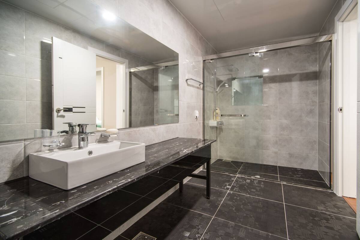 A modern bathroom with a large mirror, a white sink, and a glass-enclosed shower area.
