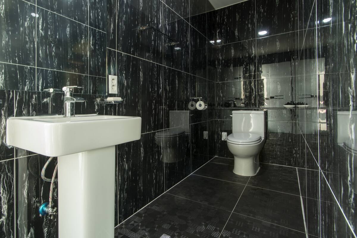 A modern bathroom with black marble walls, a white sink, and a toilet.