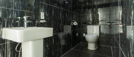 A modern bathroom with black marble walls, a white sink, and a toilet.