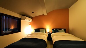 A hotel room with two beds, a window with blinds, an air conditioning unit, and a bedside table with a lamp. - Guest House Nishijin Yui (Kyoto)