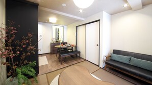 A living room with a black leather sofa, a wooden dining table with chairs, and a small bench. There is a black partition wall and a white door. - Guest House Nishijin Yui (Kyoto)