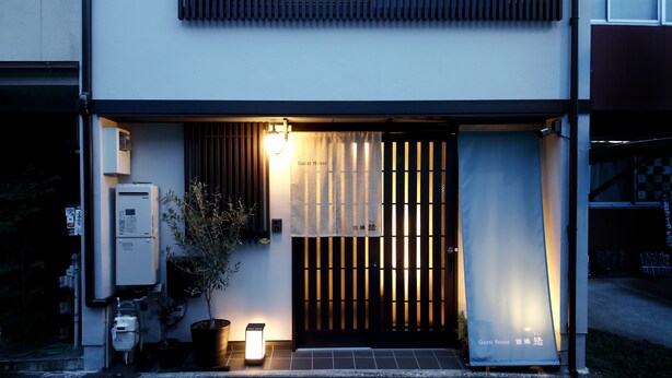 A modern building with a gated entrance, a sign reading "Guest House," and a small outdoor area with a potted plant and a light fixture. - Guest House Nishijin Yui (Kyoto)