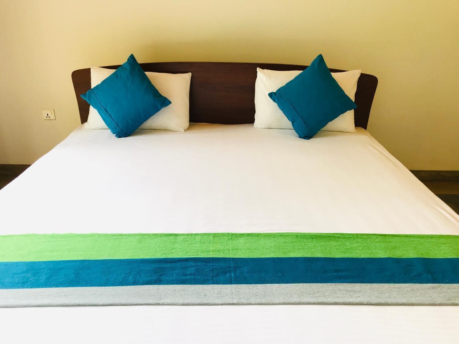 A bed with a white mattress, two blue pillows, and a green and blue striped blanket.
