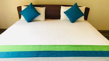 A bed with a white mattress, two blue pillows, and a green and blue striped blanket.