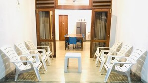 Een kamer met een centrale tafel en stoelen eromheen, houten deuren met glaspanelen en een betegelde vloer.
