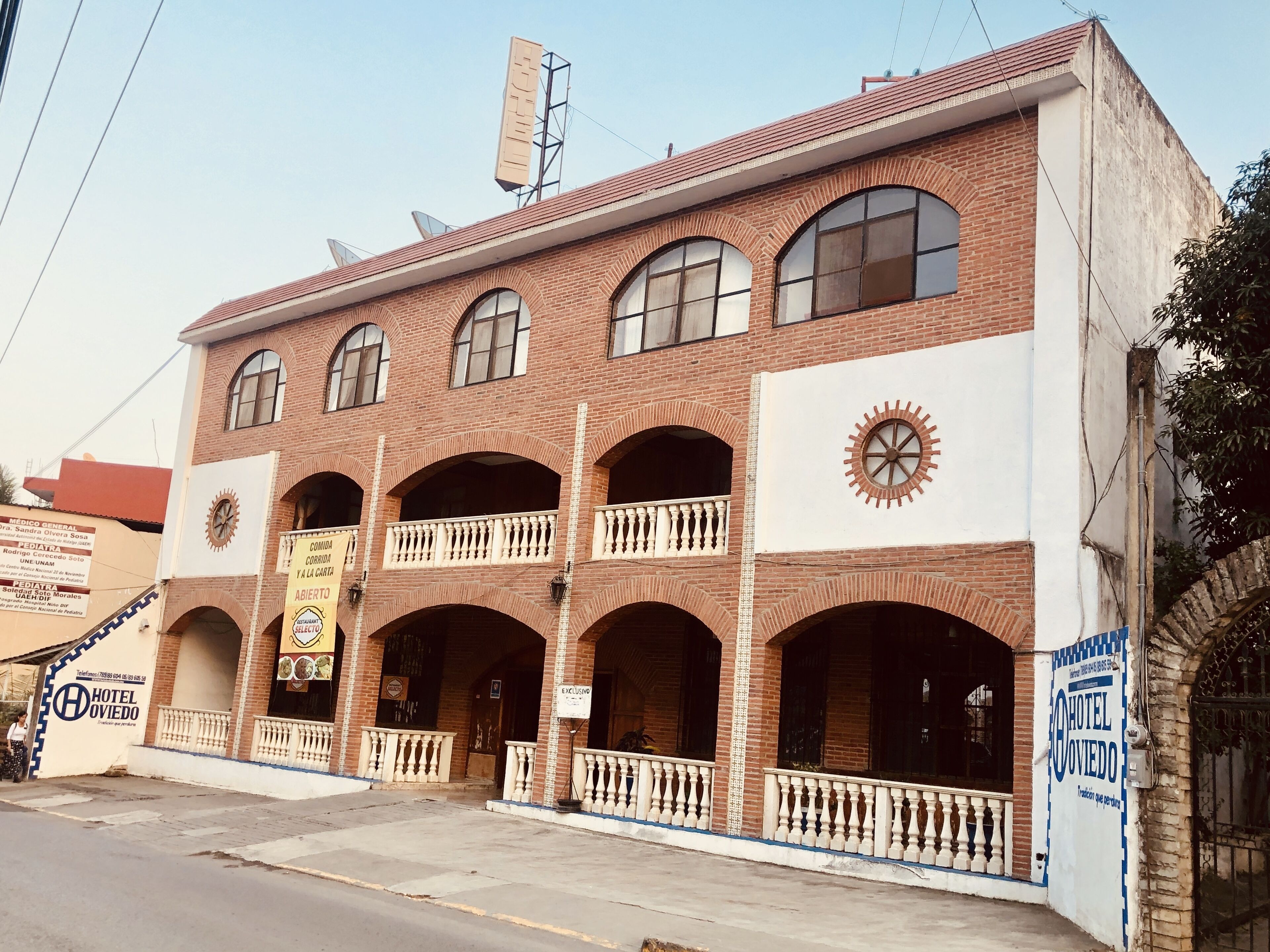 A two-story building with a brick facade, multiple balconies, and a large clock.