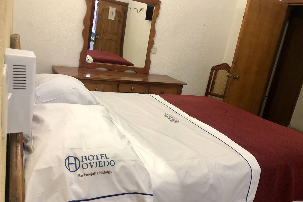 Une chambre d’hôtel avec un lit, une commode en bois, un miroir et une porte.