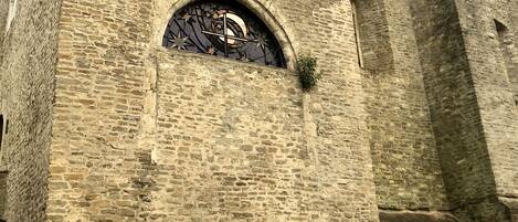 A historic stone building with a large arched window featuring a decorative metal design.
