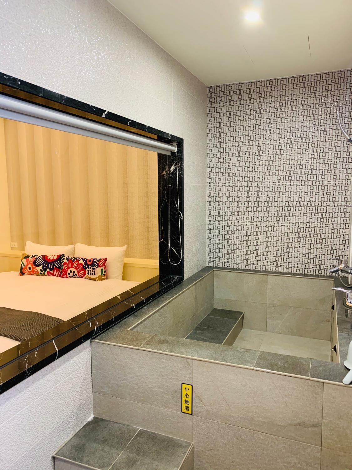A hotel room with a bed, a large mirror, a shower area, and a patterned wall.
