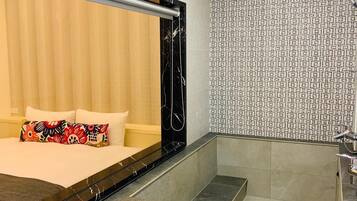 A hotel room with a bed, a large mirror, a shower area, and a patterned wall.