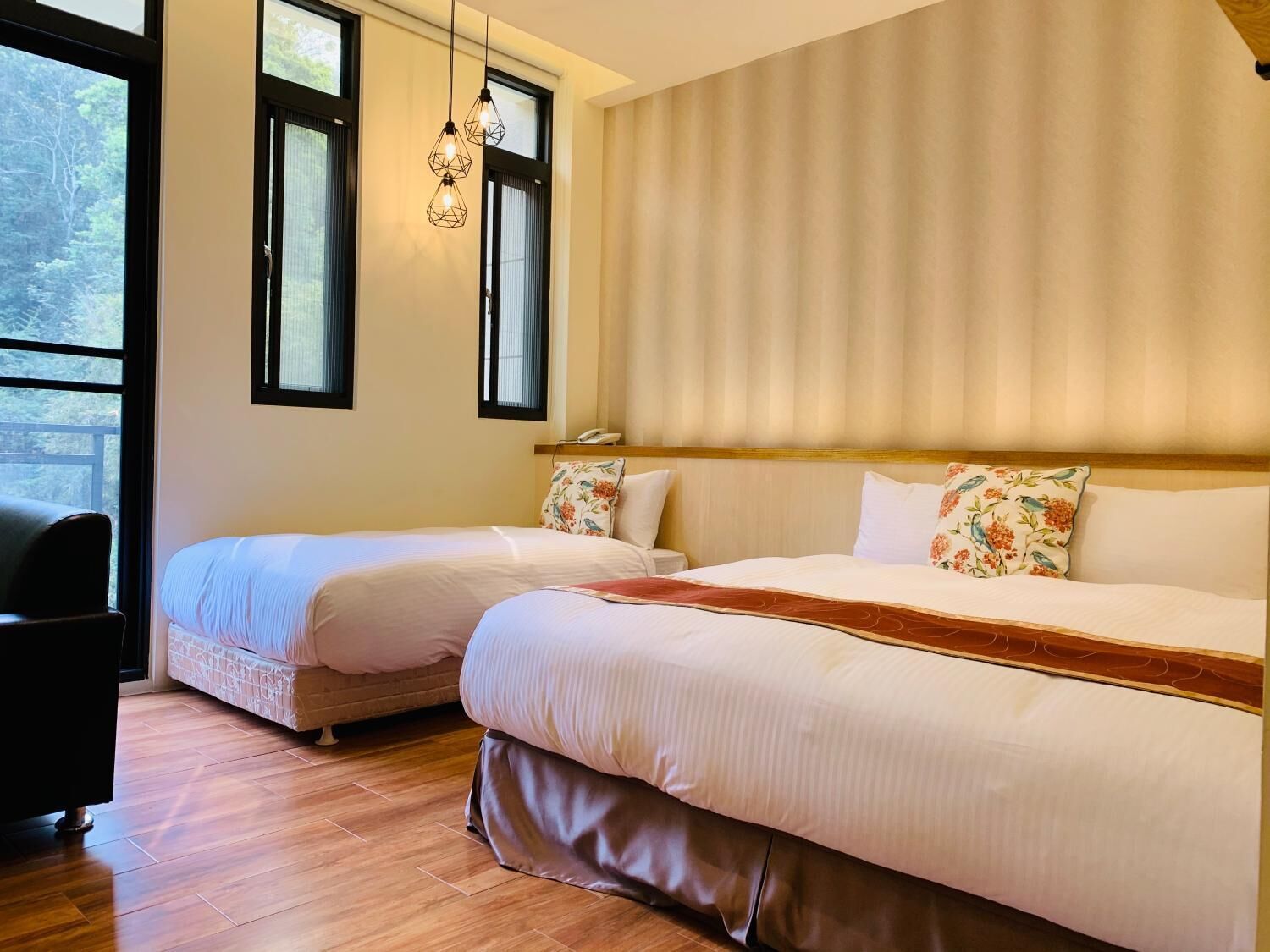 A hotel room with two beds, a wooden floor, a large window, and a hanging light fixture.