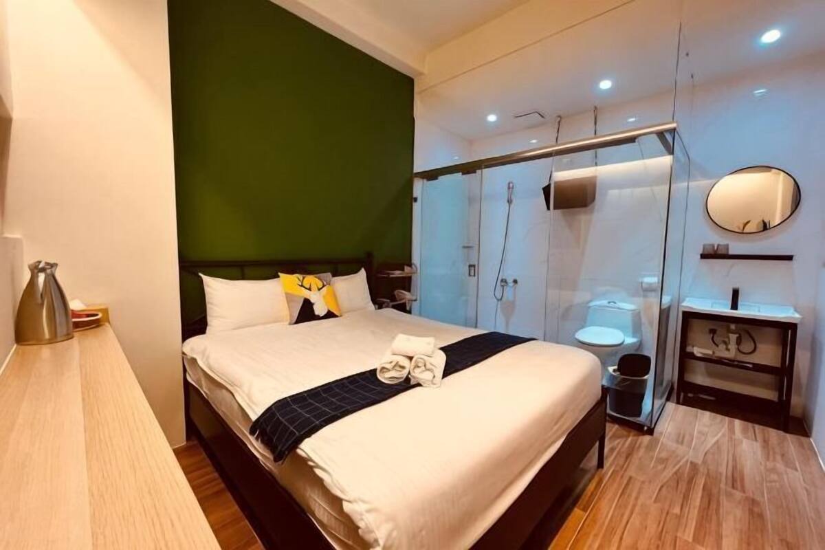 A modern hotel room with a bed, bedside table, and a glass shower enclosure.