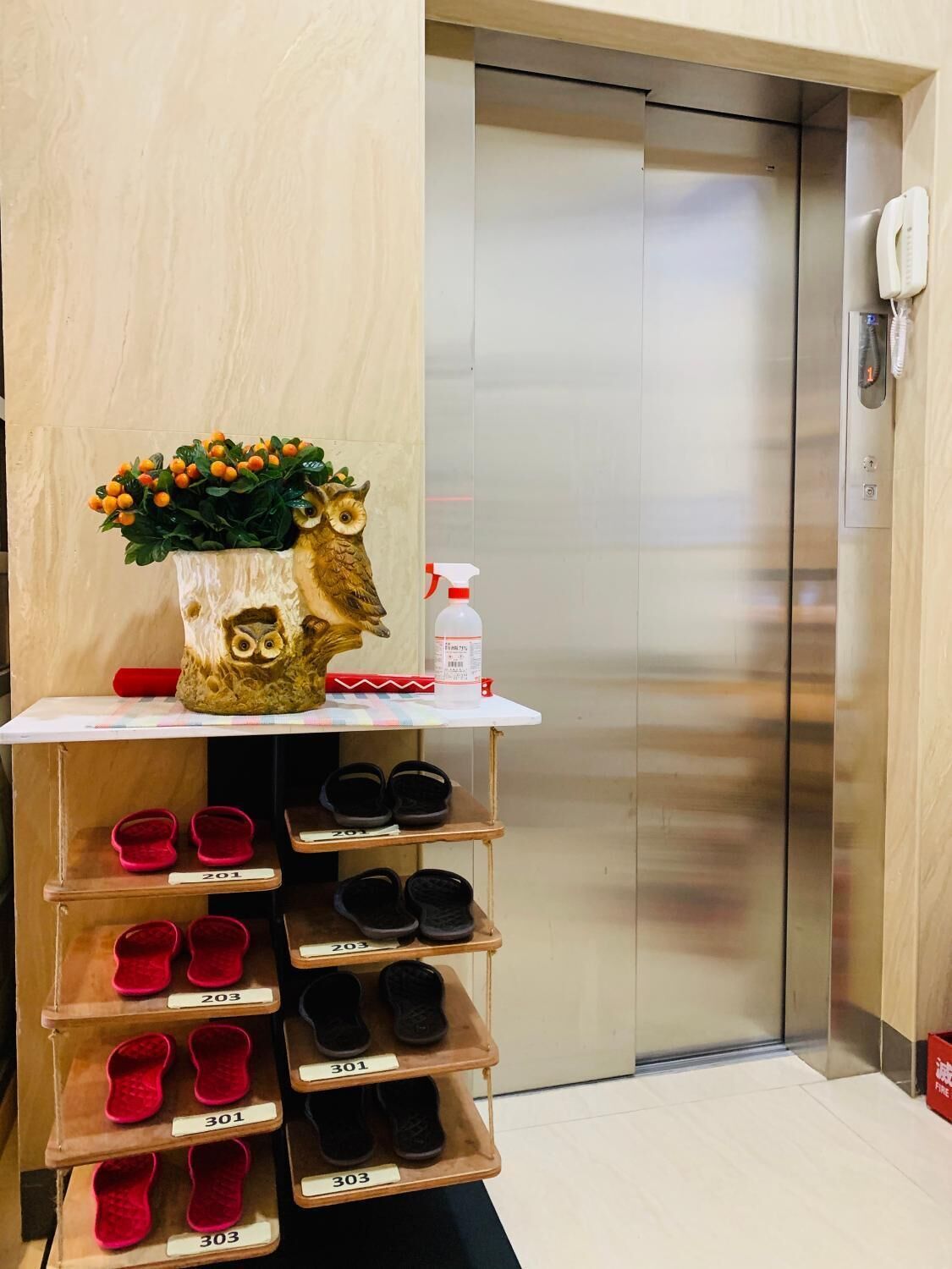 Een hotel receptie met een houten receptiebalie, een decoratief uiltje, een spuitfles en een schoenenrek met genummerde vakken.
