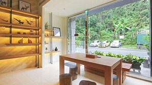 A modern interior with a wooden table and chairs, a bookshelf with various items, and a view of a road with cars and greenery outside. - Yuan Ju Boutique Hotel (Yuchi)