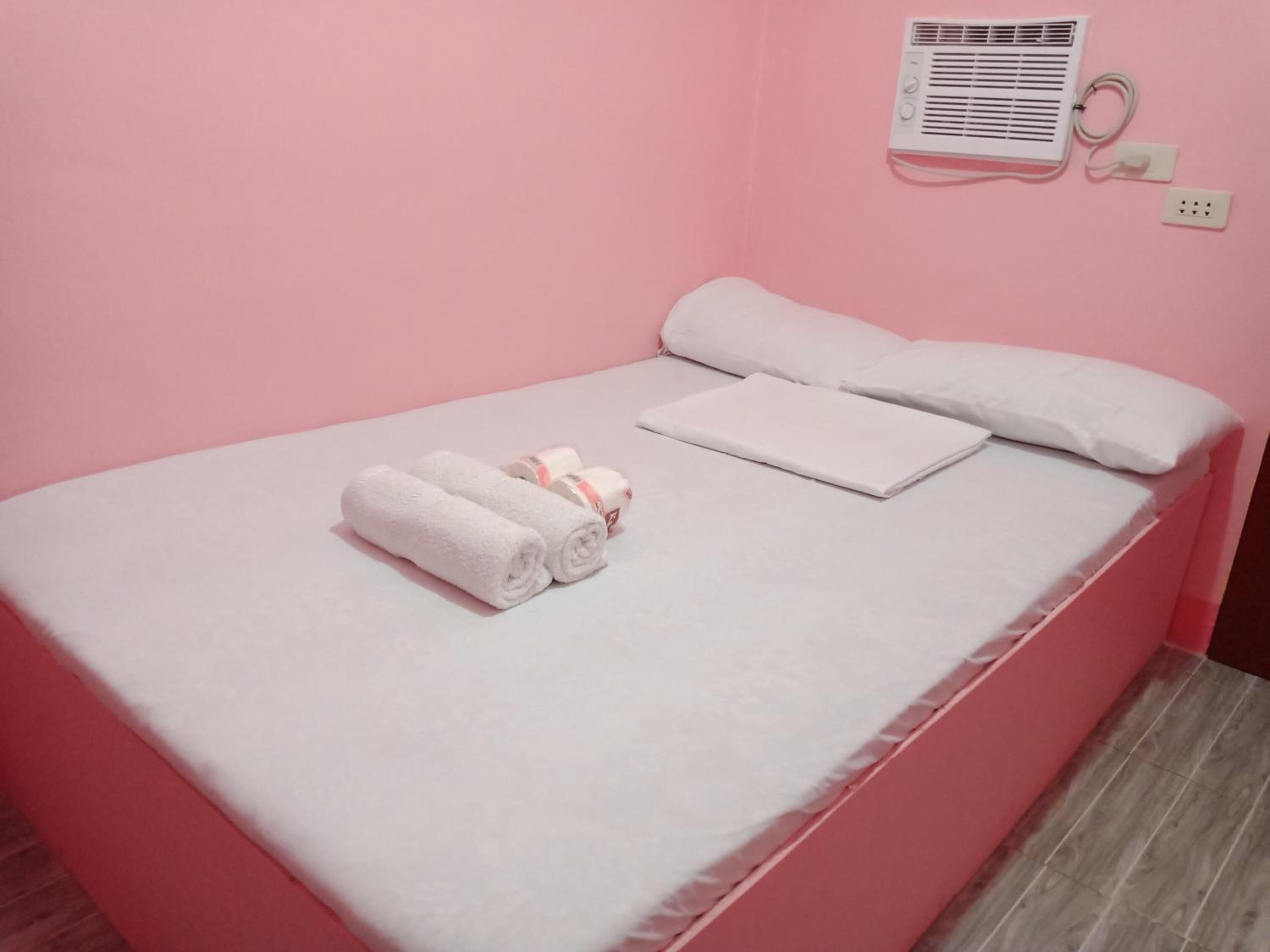 A single bed with white linens, a white pillow, and a rolled towel.