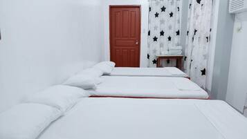 Una habitación con dos camas, ropa de cama blanca, una puerta de madera y una mesita con toallas.