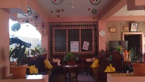 A cozy living room with a sofa, a coffee table, and various potted plants. There is a window with a metal grill and a wall clock. - Ludy's Pension House (Carles)