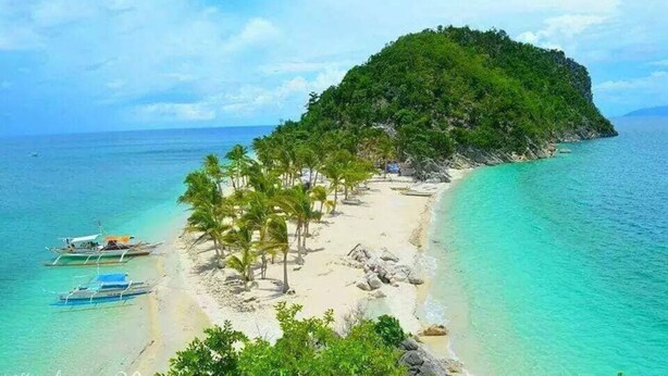 A tropical island with a sandy beach, clear turquoise waters, and a small boat docked near the shore. - Ludy's Pension House (Carles)