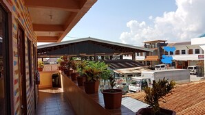 A covered outdoor area with potted plants, a tiled floor, and a view of surrounding buildings. - Ludy's Pension House (Carles)