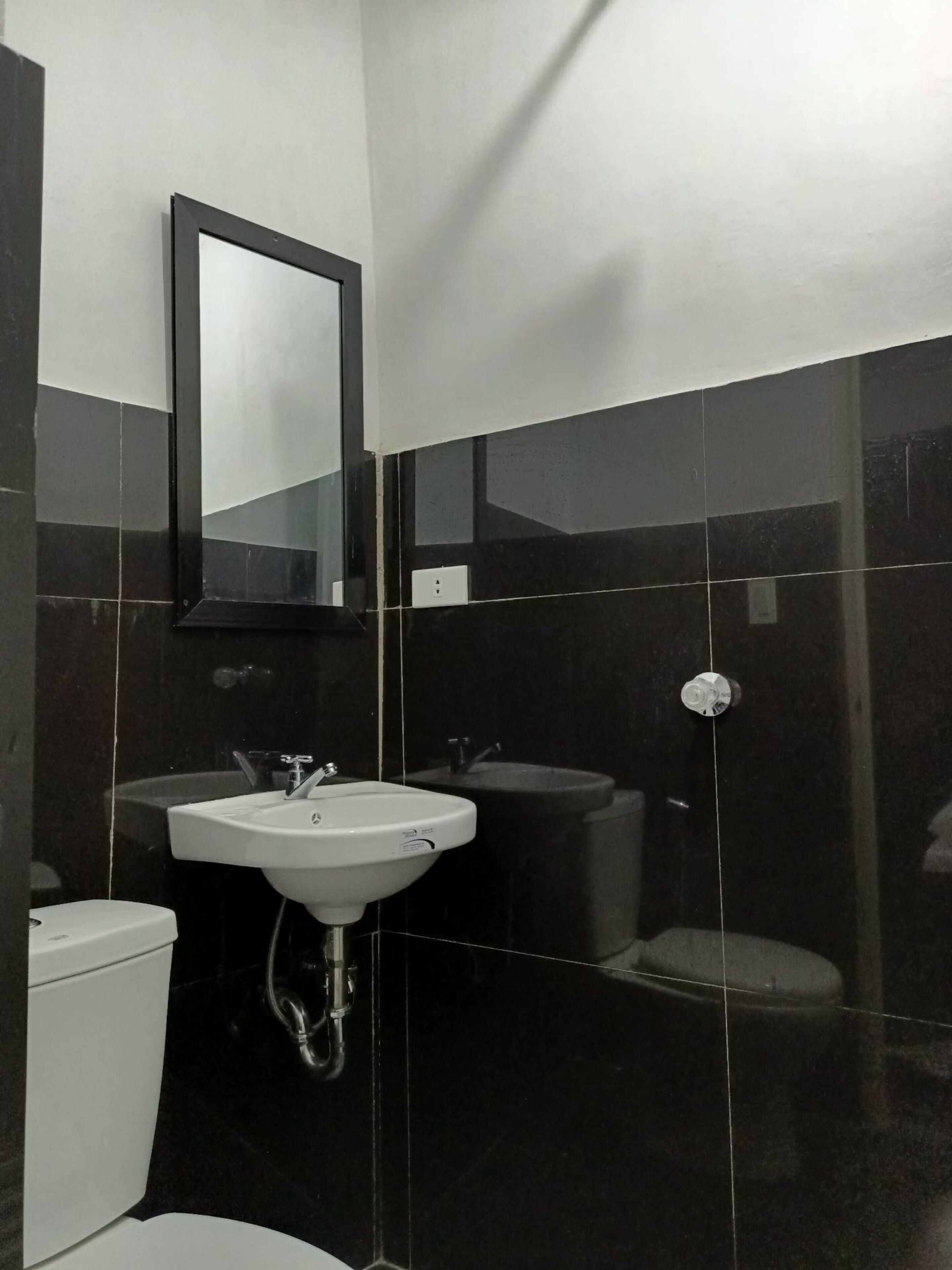 A bathroom with a white sink, two mirrors, and a black tiled wall.