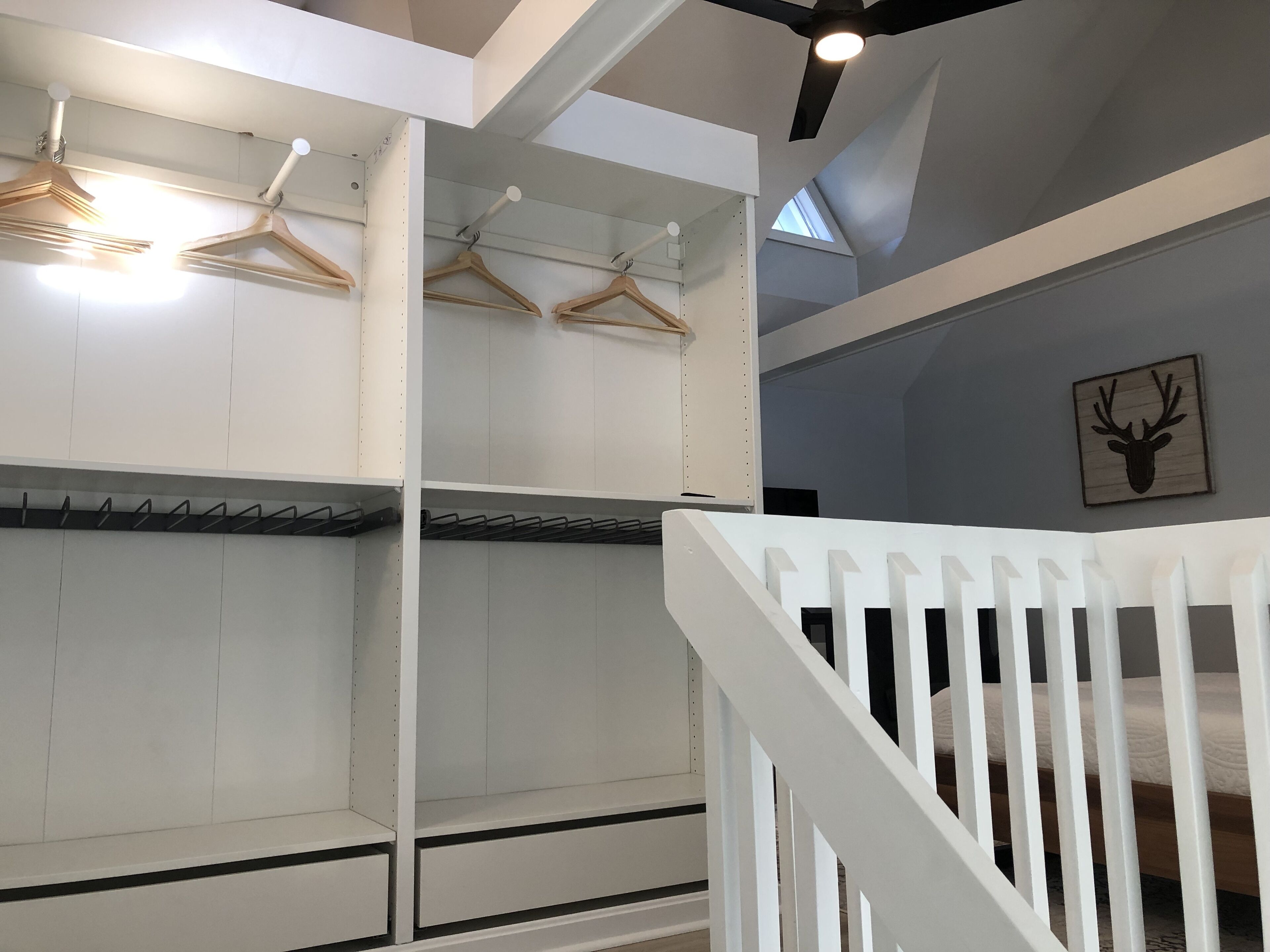 Een kamer met witte wanden, een houten plafond en een witte balustrade. Er hangen houten kledinghangers aan de muur en een decoratie van een hertenkop.