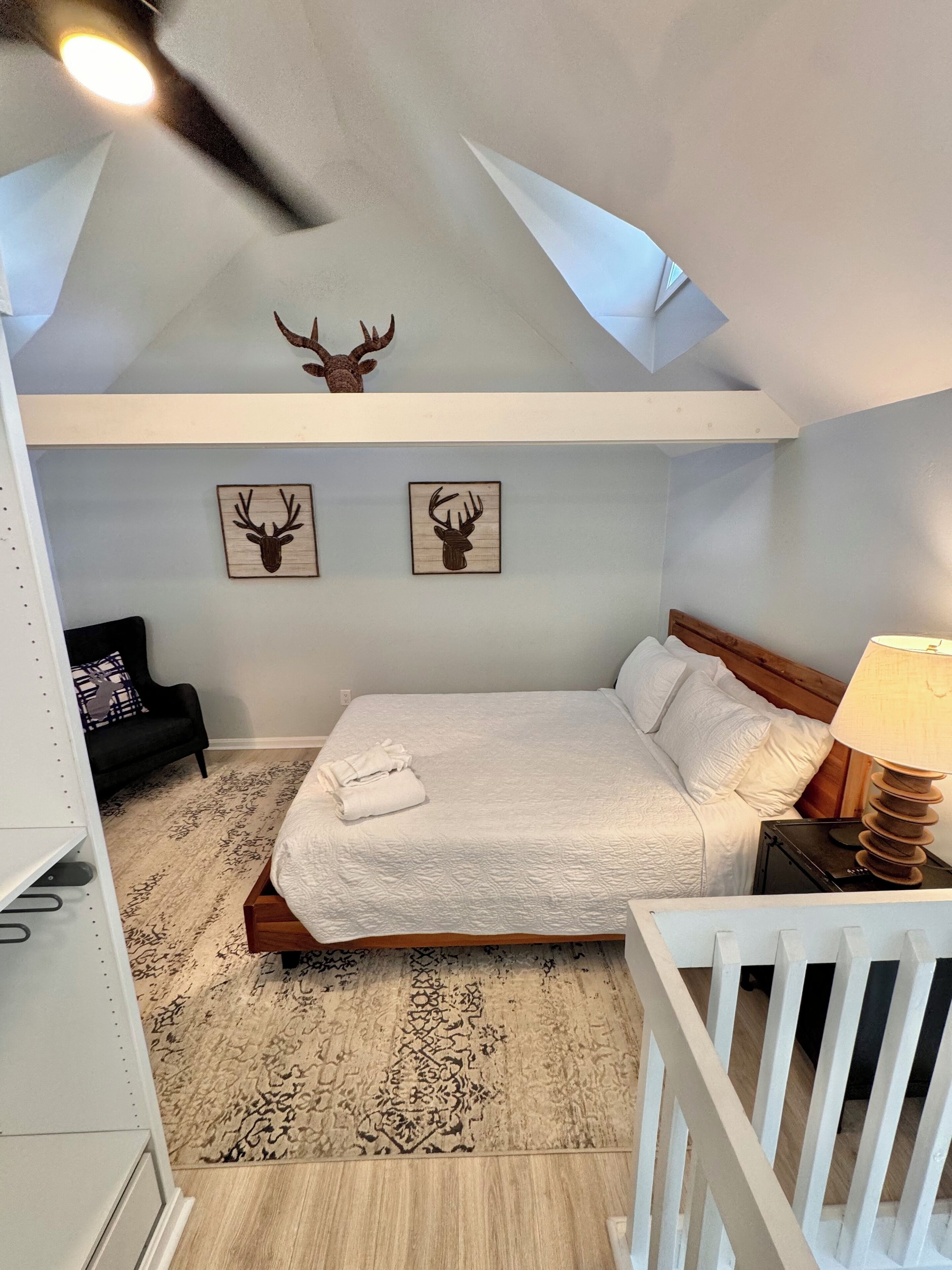 A bedroom with a bed, a nightstand, a lamp, a ceiling fan, and two deer head wall art pieces.
